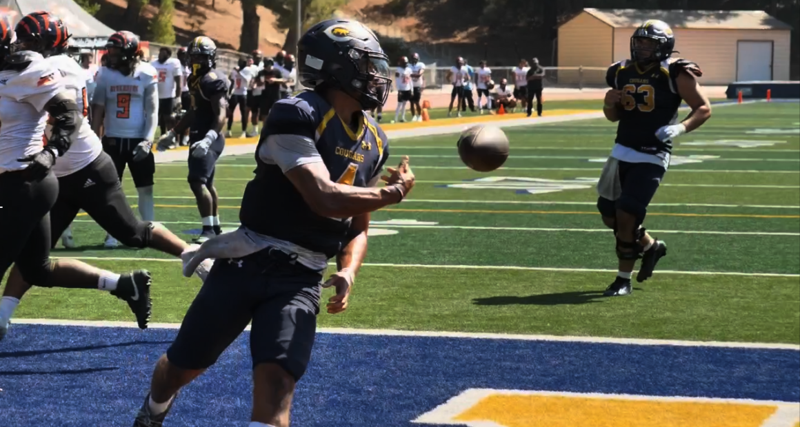 COC quarterback wearing jersey number 4 runs into the end zone holding a football before tossing it back to the referee after scoring a touchdown during the College of the Canyons vs. Riverside game on September 13, 2025, at Cougar Stadium. Other players from both teams are visible in the background on the field and sidelines.