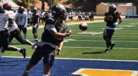 COC quarterback wearing jersey number 4 runs into the end zone holding a football before tossing it back to the referee after scoring a touchdown during the College of the Canyons vs. Riverside game on September 13, 2025, at Cougar Stadium. Other players from both teams are visible in the background on the field and sidelines.