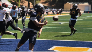 COC quarterback wearing jersey number 4 runs into the end zone holding a football before tossing it back to the referee after scoring a touchdown during the College of the Canyons vs. Riverside game on September 13, 2025, at Cougar Stadium. Other players from both teams are visible in the background on the field and sidelines.