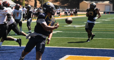COC quarterback wearing jersey number 4 runs into the end zone holding a football before tossing it back to the referee after scoring a touchdown during the College of the Canyons vs. Riverside game on September 13, 2025, at Cougar Stadium. Other players from both teams are visible in the background on the field and sidelines.