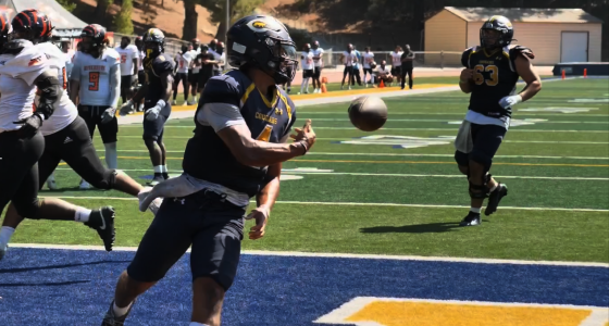 COC quarterback wearing jersey number 4 runs into the end zone holding a football before tossing it back to the referee after scoring a touchdown during the College of the Canyons vs. Riverside game on September 13, 2025, at Cougar Stadium. Other players from both teams are visible in the background on the field and sidelines.