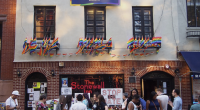 A crowd of people gathers outside The Stonewall Inn, a historic LGBTQ+ landmark in New York City. The building is decorated with numerous rainbow Pride flags and a banner above the windows that reads "#FindYourPark." Signs displayed include messages like "STOP THE HATE" and "LOVE > HATE." The scene reflects support for LGBTQ+ rights and commemorates the legacy of Stone
