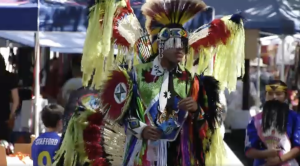 a member of the Fernandeno Tataviam Band of Mission Indians is dressed int bright yellow and red feathers with a band covering his eyes at the Hart of the West Pow Wow at HArt park