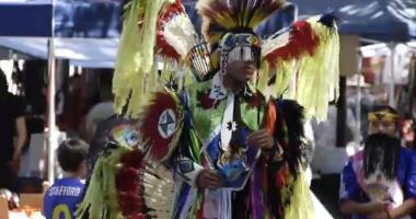 a member of the Fernandeno Tataviam Band of Mission Indians is dressed int bright yellow and red feathers with a band covering his eyes at the Hart of the West Pow Wow at HArt park