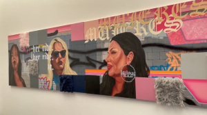 A colorful mural featuring portraits of three women against a backdrop of graffiti-style art and text. The piece includes bold pink, gray, and blue tones with textured fabric squares attached to the surface. One woman wears large hoop earrings that read “Lady Lowrider,” and the background includes stylized lettering and the phrase “her ride.”