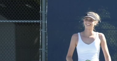 Freshman tennis player Emma Chodur’s wearing a white tank top and dark hat holding a tennis racket smiles while standing on a tennis court at college of the canyons.