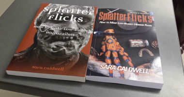 Two books titled Splatter Flicks: How to Make Low-Budget Horror Films by Sara Caldwell are placed side by side on a gray surface. The book on the left has a red cover featuring a close-up of a zombie-like face in black and white. The book on the right, labeled “Revised & Expanded,” shows a cover with a monster hand prop, a jar of preserved objects, and prosthetic teeth on a dark background.