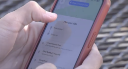 A person holds a smartphone with a red case, using a ride-planning app that displays “Plan your ride” and location options such as “Canyon Country Park” and “17615 Soledad Canyon Rd” on the screen.