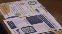 Flyers for college student support services lie on a table. One flyer promotes health and wellness workshops and includes a QR code, colorful graphics, and contact information. Another flyer advertises “The Basic Needs Center,” listing office hours, campus locations, available resources such as food assistance and school supplies, and another QR code. Social media icons and program details are visible across the pages.