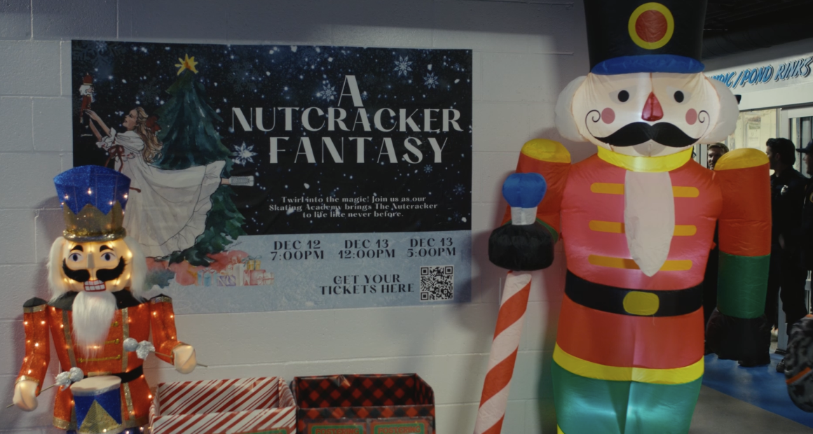 “A holiday display featuring two large nutcracker decorations—one illuminated with glittering lights on the left and a tall inflatable nutcracker on the right. Between them is a poster for ‘A Nutcracker Fantasy,’ showing a girl placing a nutcracker ornament on a Christmas tree. The poster lists showtimes for December 12 and 13 and includes a QR code for tickets. Gift-wrapped donation boxes sit below the poster, and people are visible in the background near an entrance.”
