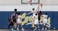 Alt text: College of the Canyons men’s basketball players in white leap to contest a shot at the rim as an opposing player in a black jersey attempts a layup, with multiple players watching beneath the basket inside a gym.