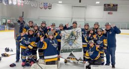 **Alt text:** A youth girls hockey team in blue and gold uniforms poses on the ice with coaches, smiling and raising one finger while holding a banner that reads “Hockey House 2025–26 Playoff Champions” inside an indoor rink.