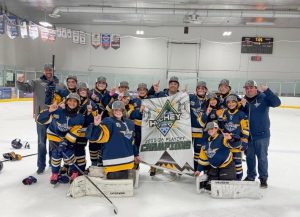 **Alt text:** A youth girls hockey team in blue and gold uniforms poses on the ice with coaches, smiling and raising one finger while holding a banner that reads “Hockey House 2025–26 Playoff Champions” inside an indoor rink.