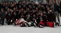 University of New Mexico Lobos in black and red uniforms poses on the ice with a championship trophy, celebrating at The Cube rink after a playoff win