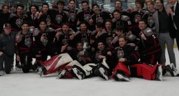 University of New Mexico Lobos in black and red uniforms poses on the ice with a championship trophy, celebrating at The Cube rink after a playoff win