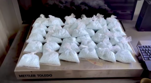 Dozens of small clear plastic bags filled with light blue pills are arranged in rows on a tabletop scale labeled “Mettler Toledo,” with a computer keyboard partially visible to the side.