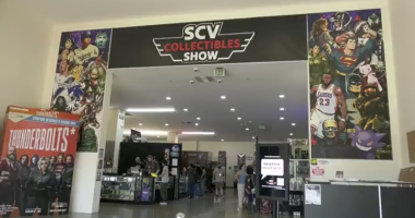 Entrance to the SCV Collectibles Show inside a convention hall, with large posters of comic book and pop culture characters on either side and vendors and attendees visible inside.
