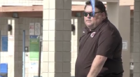 A Sean Kakumu sunglasses and a dark polo shirt stands outdoors near tiled columns and a railing, with a blue object partially obscuring the foreground.