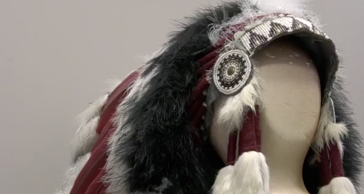 This image features a Native American-style headdress displayed on a neutral-toned mannequin head. The piece is highly detailed, showcasing traditional craftsmanship through various textures and materials.