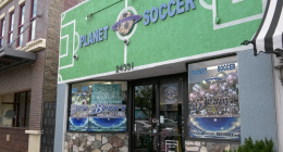 The storefront of Planet Soccer features a bright green facade with a soccer field design, large signage above the entrance, and window displays filled with soccer gear and promotional posters.