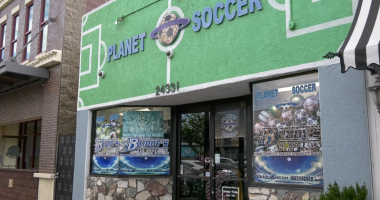 The storefront of Planet Soccer features a bright green facade with a soccer field design, large signage above the entrance, and window displays filled with soccer gear and promotional posters.