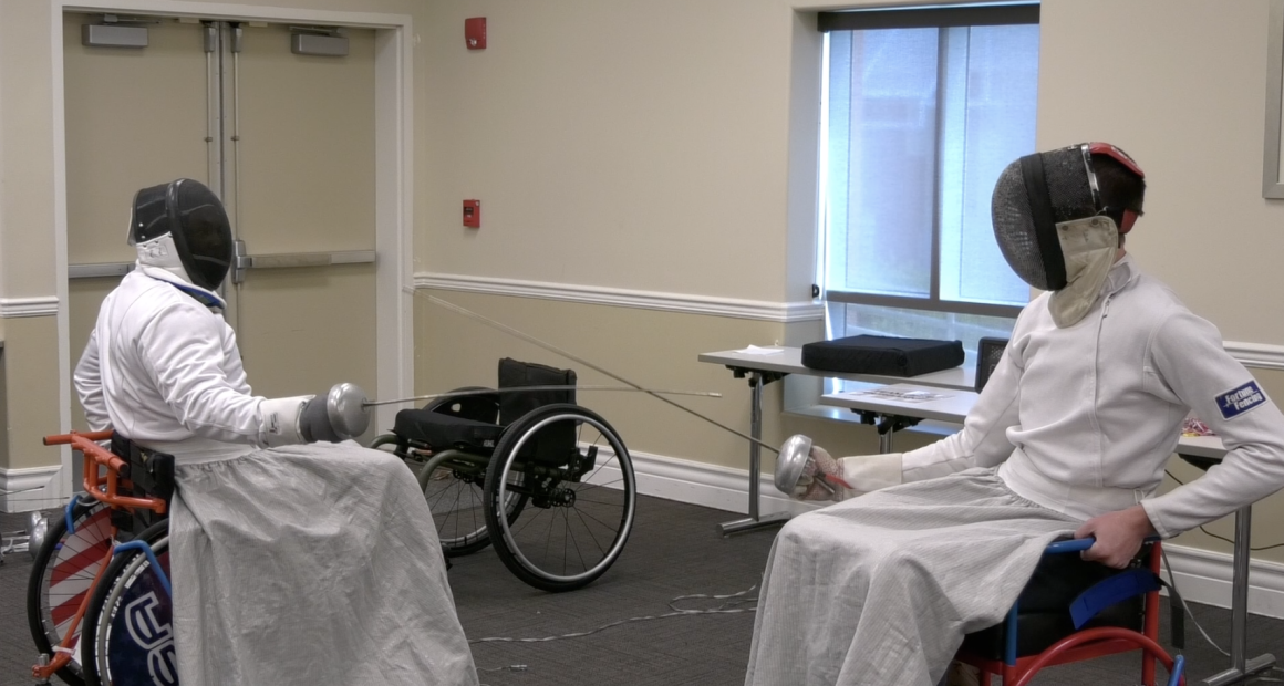 Two wheelchair fencers in protective gear face off with foils during a match, demonstrating adaptive sports at the Triumph Foundation’s Wheelchair Sports Festival.