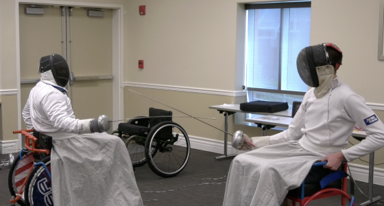 Two wheelchair fencers in protective gear face off with foils during a match, demonstrating adaptive sports at the Triumph Foundation’s Wheelchair Sports Festival.